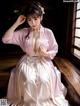 A woman in a pink and white dress sitting on a wooden bench.