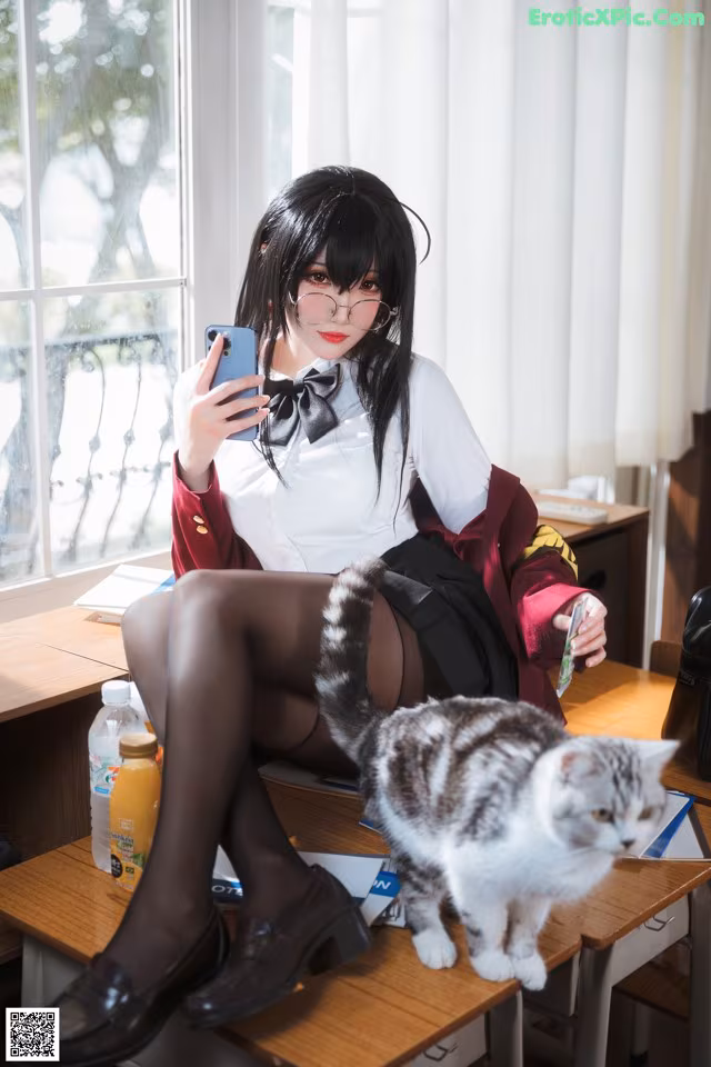 A woman sitting at a desk with a cat and a cell phone.
