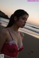 A woman in a red bra and panties standing on a beach.